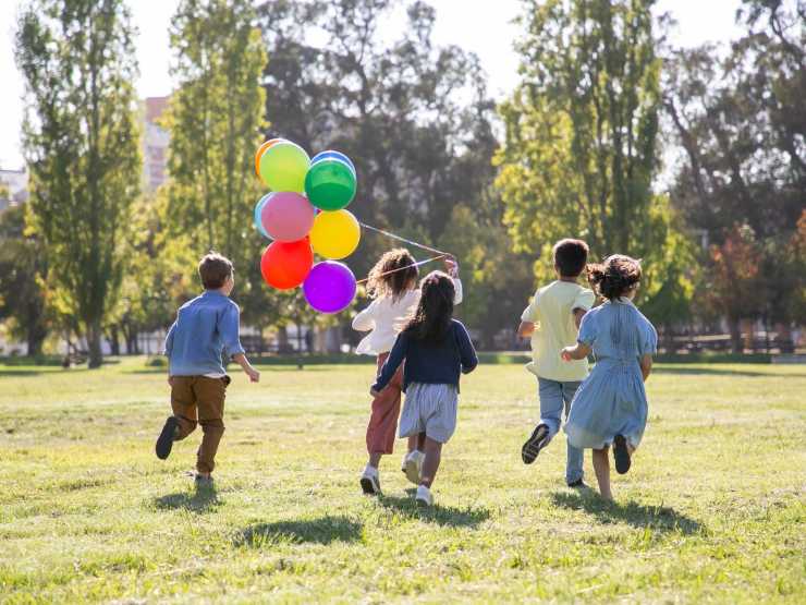 bambini che corrono sul prato con palloncini